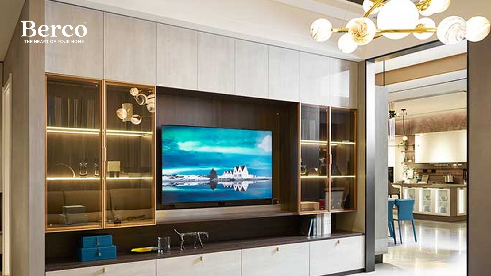 Media wall with brass-framed glass display cabinets lit shelf by shelf, a dark centre panel behind the screen and a long low drawer run — Berco design reference.